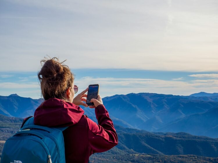 Como procuro tirar fotos melhores em viagens usando só o celular 11 Mulher fotografa uma paisagem de montanha com o celular durante uma viagem.