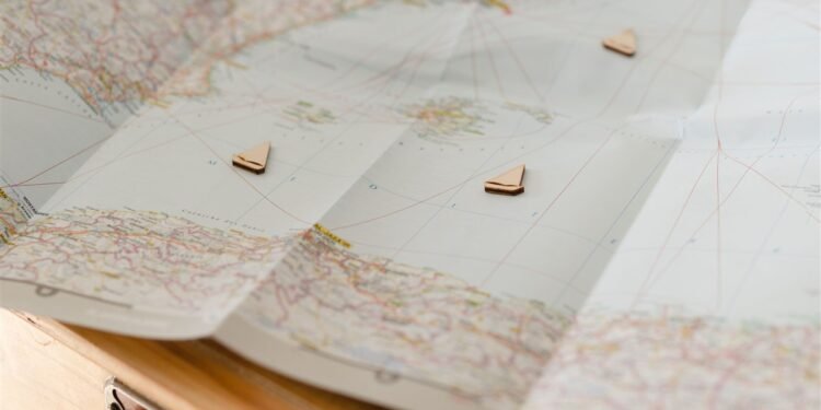 Mapa dobrado sobre uma mesa com pequenos marcadores em forma de barco indicando pontos de um roteiro de viagem.
