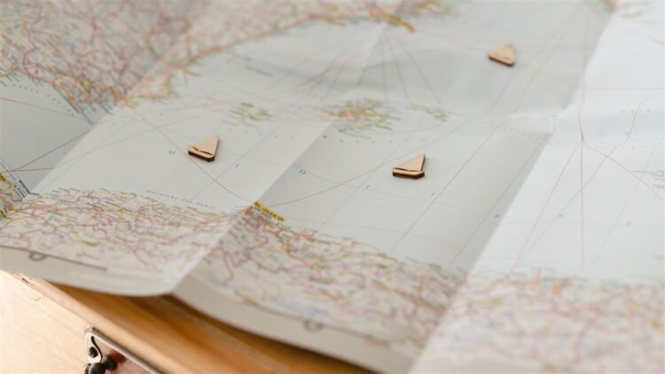 Como escolher onde se hospedar em uma cidade que você não conhece 11 Mapa dobrado sobre uma mesa com pequenos marcadores em forma de barco indicando pontos de um roteiro de viagem.