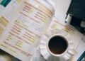 Caderno com anotações de conjugação verbal em espanhol, xícara de café ao lado, sobre uma mesa de estudo.