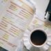 Caderno com anotações de conjugação verbal em espanhol, xícara de café ao lado, sobre uma mesa de estudo.