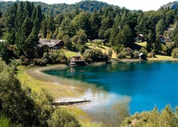 Vista de Llao Llao em Bariloche, com lago azul, vegetação e casas entre as montanhas.