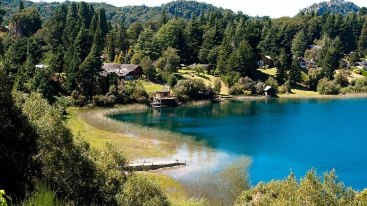 Vista de Llao Llao em Bariloche, com lago azul, vegetação e casas entre as montanhas.