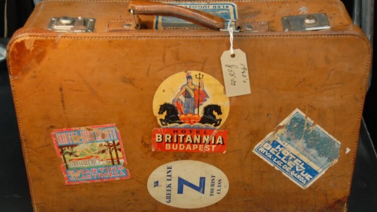 Acessórios de viagem que realmente valem espaço na mala 11 Mala de couro vintage coberta de etiquetas antigas de hotéis e companhias de viagem.
