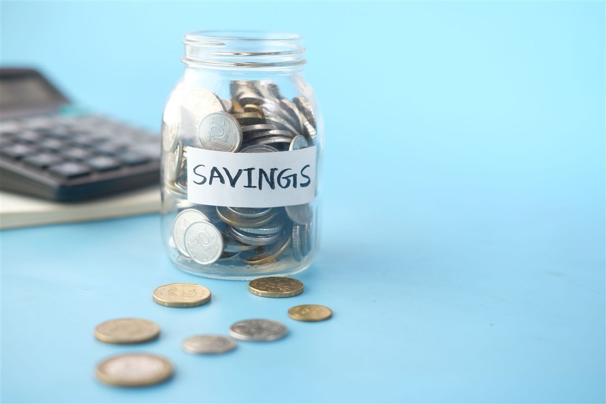 Pote com moedas e etiqueta "Savings" ao lado de uma calculadora.