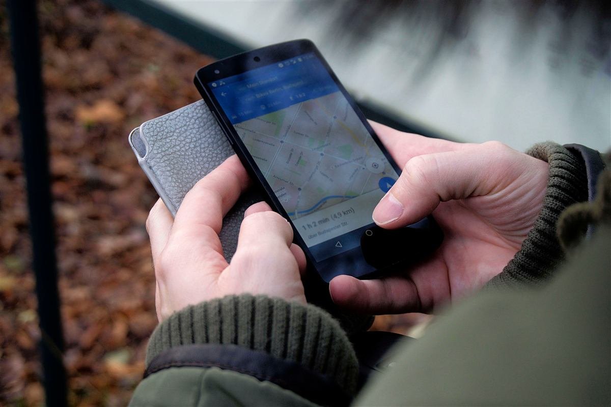 Mãos segurando um smartphone e conferindo uma rota num aplicativo de mapa.