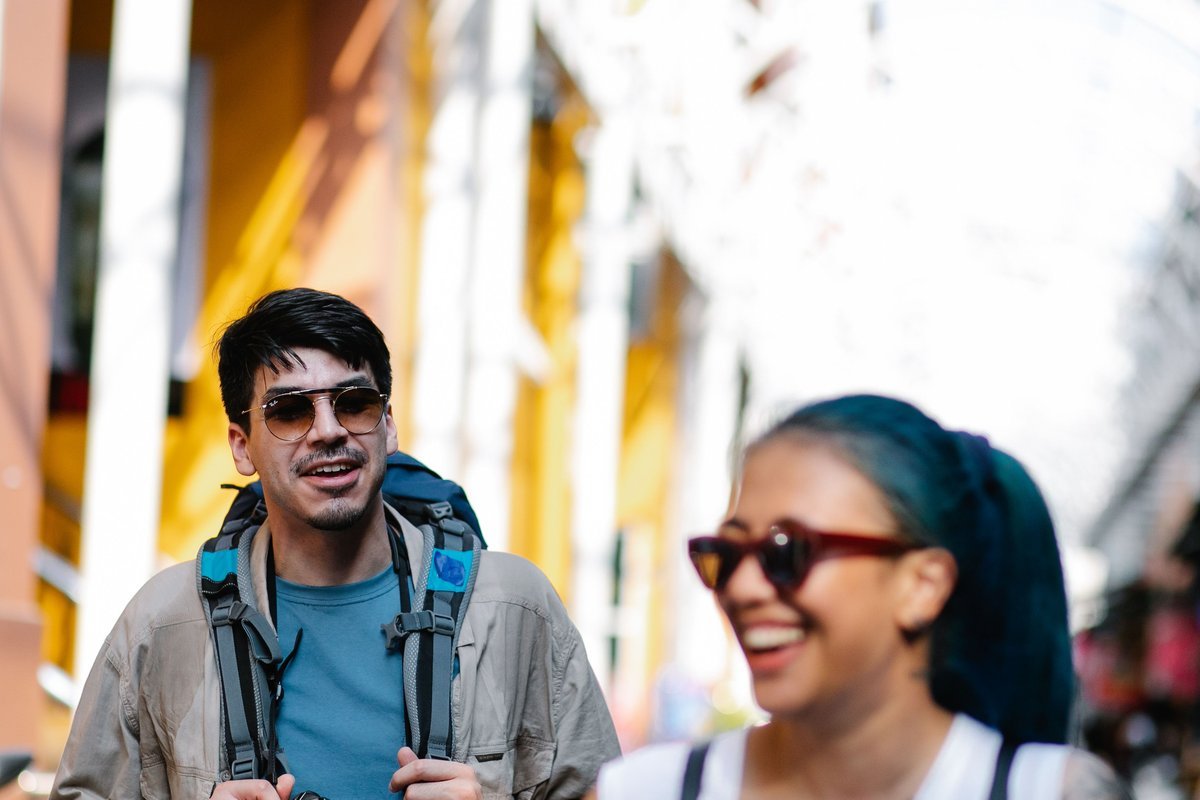 Duas pessoas com mochilas conversam em uma rua colorida.
