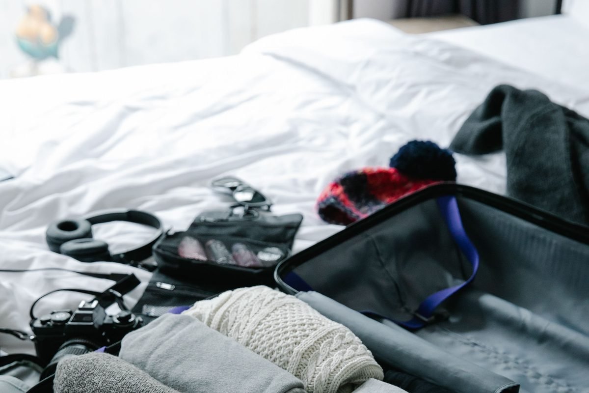 Mala aberta sobre uma cama, com roupas dobradas e organizadas ao lado de uma câmera e outros itens de viagem.