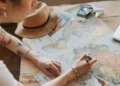 Pessoa marca um mapa-múndi em uma mesa com itens de viagem.