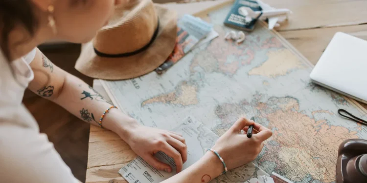 Pessoa marca um mapa-múndi em uma mesa com itens de viagem.