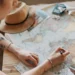 Pessoa marca um mapa-múndi em uma mesa com itens de viagem.