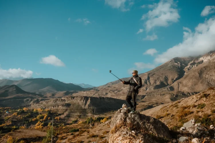 Viajante tirando selfie com bastao em paisagem de montanha