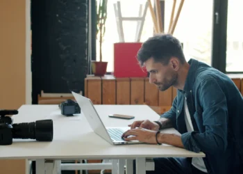 Fotógrafo edita imagens em um laptop, com uma câmera sobre a mesa.