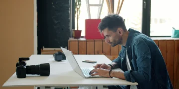 Fotógrafo edita imagens em um laptop, com uma câmera sobre a mesa.