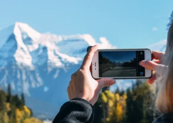 Pessoa fotografa com o celular uma estrada em direção a montanhas nevadas.
