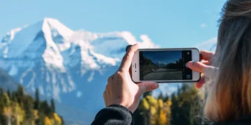 Pessoa fotografa com o celular uma estrada em direção a montanhas nevadas.