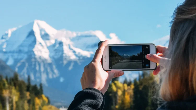 Pessoa fotografa com o celular uma estrada em direção a montanhas nevadas.