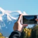 Pessoa fotografa com o celular uma estrada em direção a montanhas nevadas.